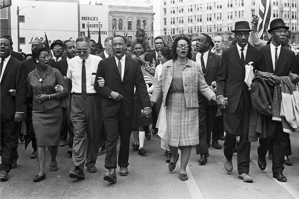 MLK leading the crowd and participants on front row walking arm in arm or hand in hand
